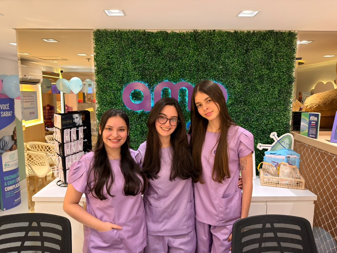 Equipe da Amo Vacinas Eldorado sorrindo em frente ao painel verde